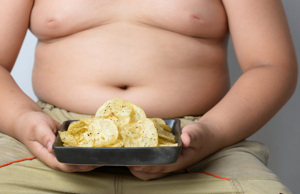 Criança obesa com um prato de batata frita em referência à obesidade infantil.