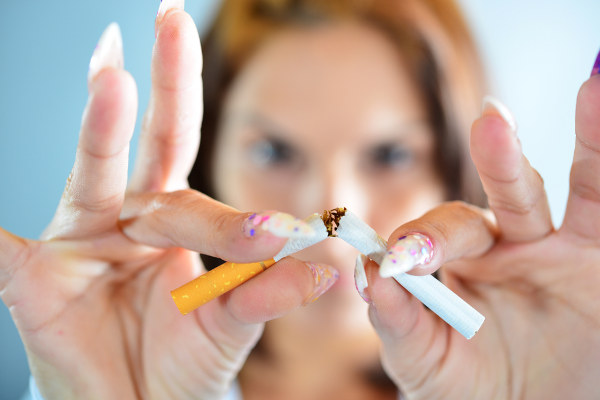 Mulher quebrando um cigarro ao meio em referência ao Mulher abraçando paciente com câncer em referência ao Dia Nacional de Combate ao Câncer.