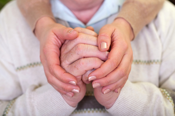 Pessoa segurando as mãos de um idoso em referência ao Alzheimer.