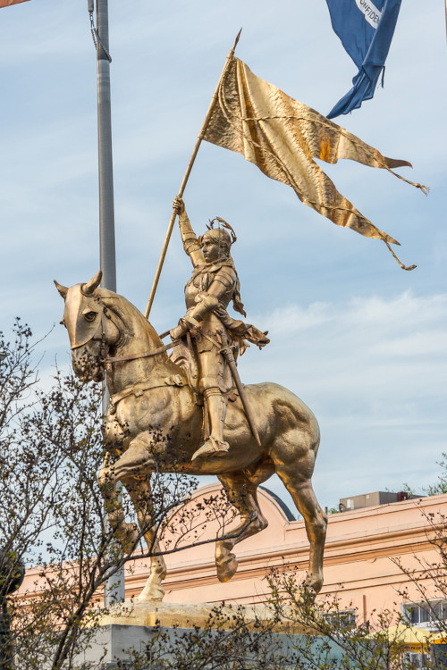 Estátua dourada retratando Joana d’Arc em cima de um cavalo e segurando uma bandeira.