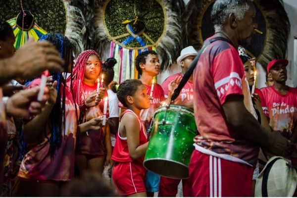 Foto de pessoas celebrando o bumba meu boi no Maranhão, com percussão e velas.