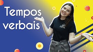 "Tempos verbais" escrito sobre fundo colorido ao lado da imagem da professora