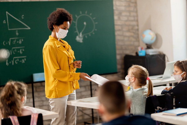 Professora e alunos em sala de aula e usando máscara.