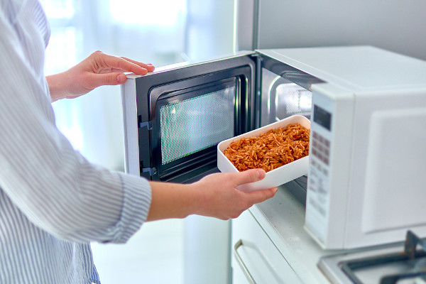 Pessoa inserindo alimento no aparelho de micro-ondas.