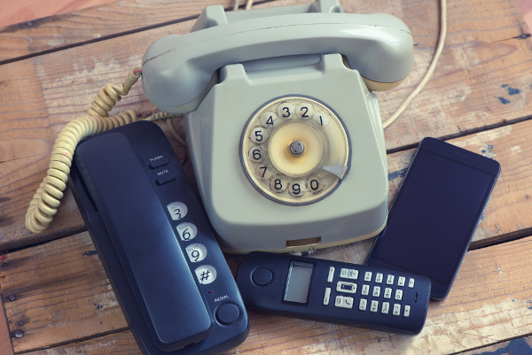 Telefones de diferentes épocas, dispostos em superfície de madeira, representando a evolução do aparelho