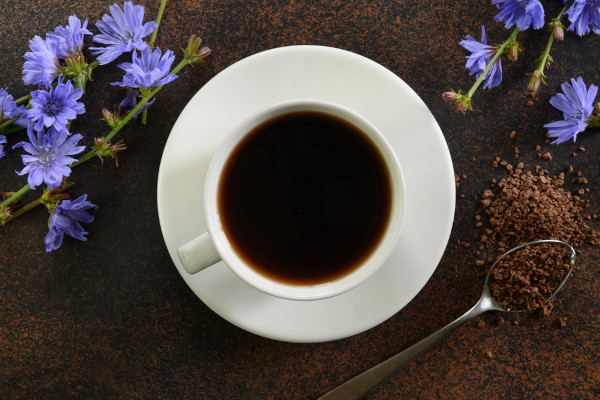 Xícara com café acompanhada de raiz de almeirão e flores roxas