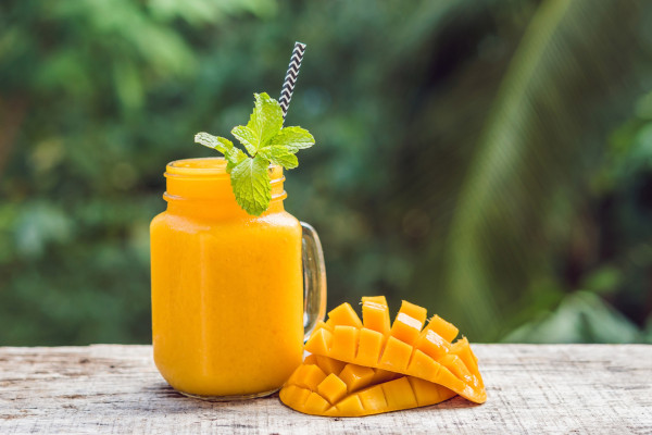 Jarra de suco de manga com pedaços de manga ao lado em superfície de madeira