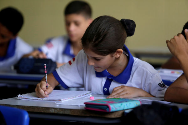Menina escrevendo em caderno em um ambiente escolar.