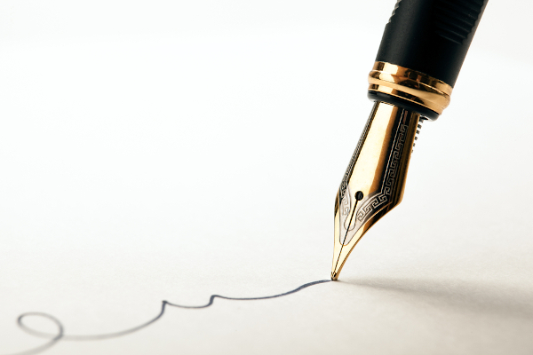 Visão aproximada de uma caneta-tinteiro sendo usada para escrever no papel.