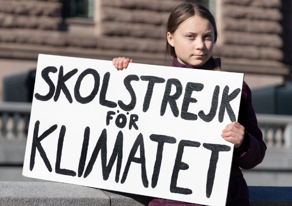Greta Thunberg manifestando-se em Estocolmo segurando uma placa que diz “Greve escolar pelo clima”.