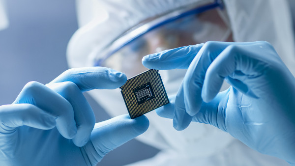 Um cientista da área tecnológica utilizando equipamentos de proteção ao segurar um microchip.