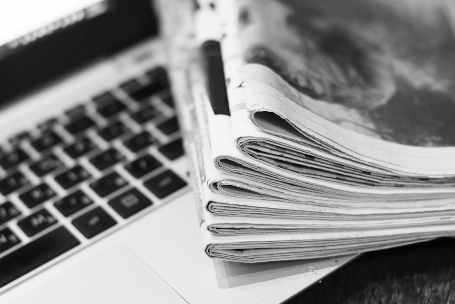 Pilha de jornais sobre notebook em referência à crônica argumentativa.