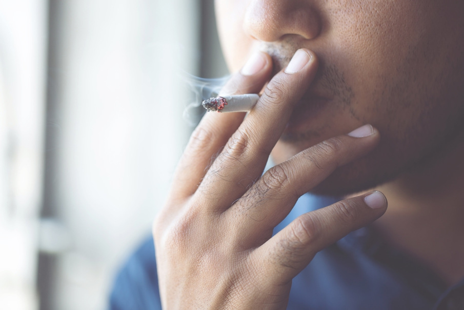 Vista aproximada de um jovem levando um cigarro à boca.