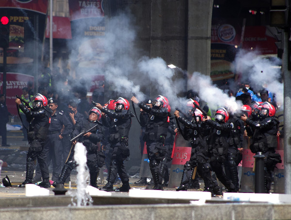 Policiais lançando gás lacrimogênio em direção a manifestantes em protesto.[1]
