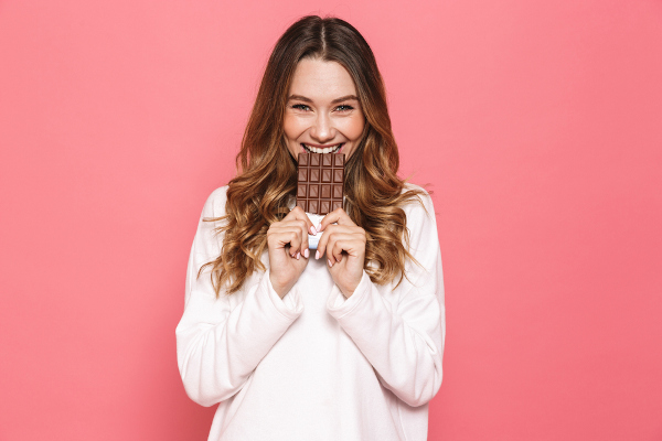  Mulher segurando barra de chocolate e simulando estar comendo-o