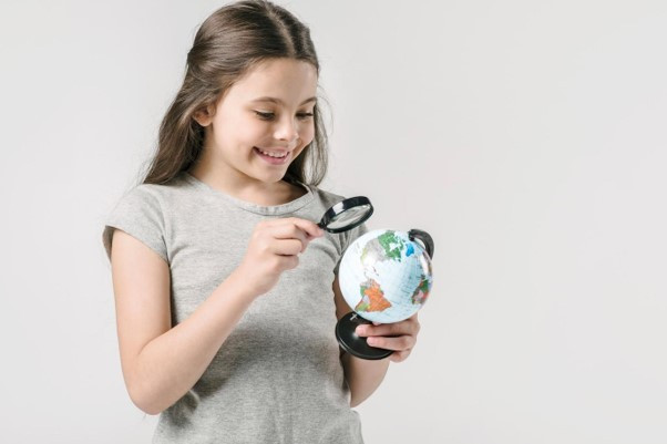 Menina olhando um mini mapa-múndi com uma lupa.