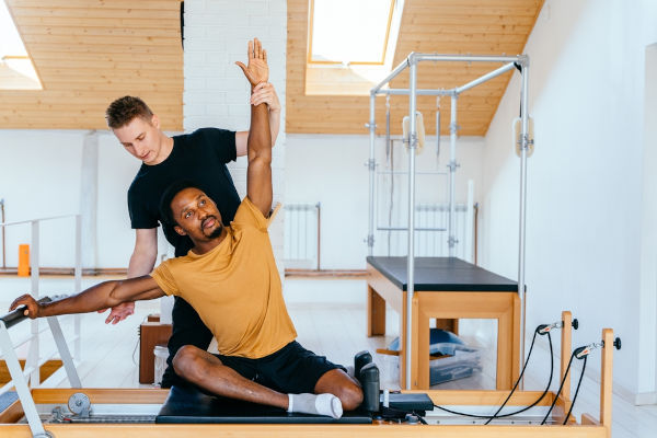 Homem praticando pilates com ajuda de um professor.