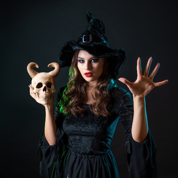 Mulher com vestido e chapéu escuros segurando caveira.