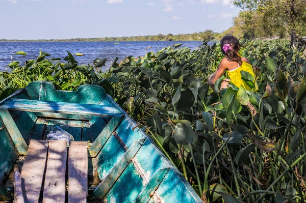 Menina sentada perto de um pequeno barco de pesca e em frente ao rio Paraguai.