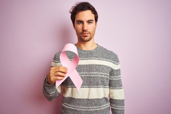 Homem segurando laço cor-de-rosa que é símbolo da luta contra o câncer de mama.
