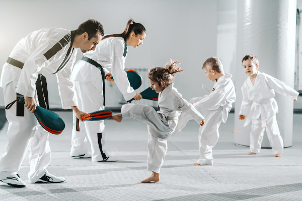 Crianças chutando em raquete de taekwondo durante a aula.