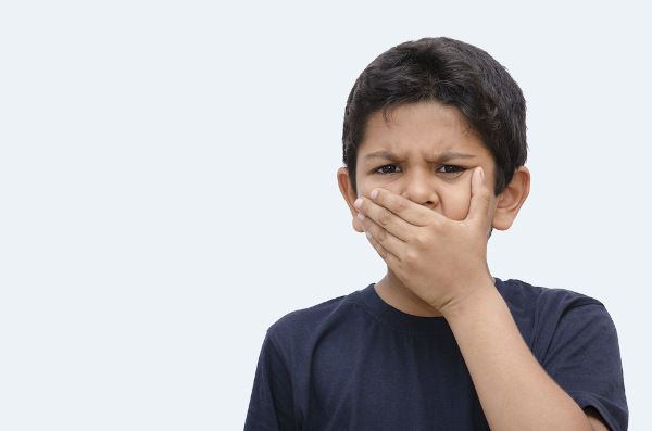 Menino com a mão sobre a boca para não proferir algumas palavras; esse impulso é um sintoma da síndrome de Tourette.