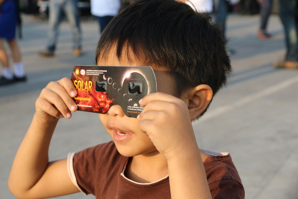 Menino vendo eclipse solar com filtro de proteção em Chiang Mai, na Tailândia.