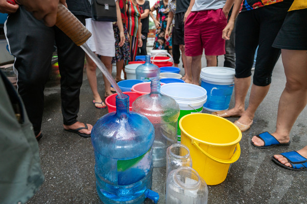  Fila de pessoas com baldes devido ao desabastecimento, uma consequência do desperdício de água.