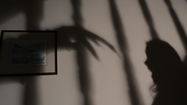 Pelas sombras projetadas em uma parede, vê-se a mão do bicho-papão perseguindo uma criança.