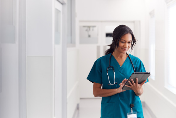 Médica, parte importante da População Economicamente Ativa (PEA), analisando o prontuário de um paciente em um tablet.