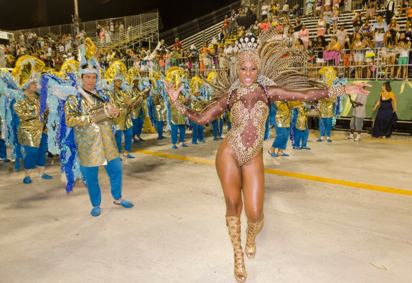 Rainha de bateria sambando pela escola de samba Vila Mathias, com a bateria ao fundo, durante o Carnaval.