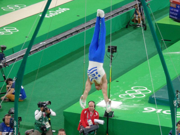 Atleta de cabeça para baixo em posição estendida nas argolas, modalidade da ginástica artística.