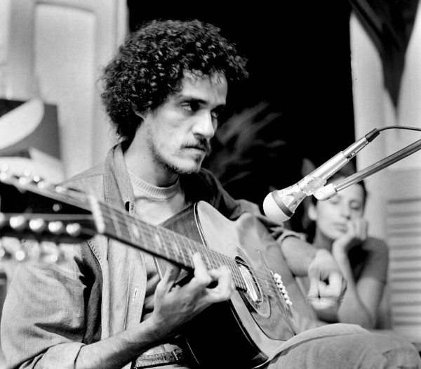 Fotografia em preto e branco mostrando Zé Ramalho jovem tocando violão. 