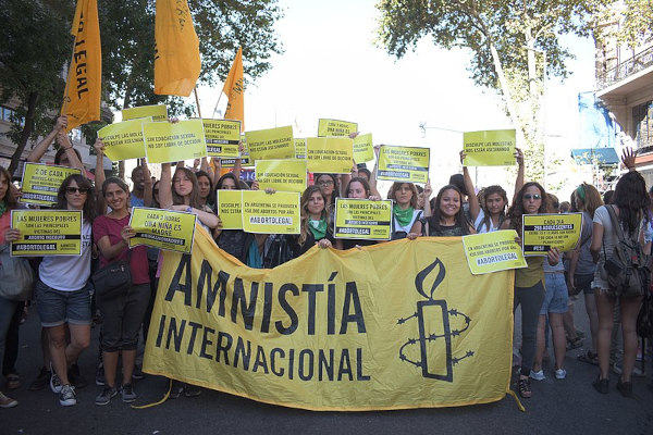 Mulheres com faixas e cartazes durante campanha da Anistia Internacional.