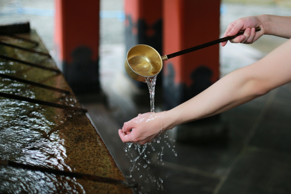 Pessoa lavando as mãos na entrada de um templo do xintoísmo. 