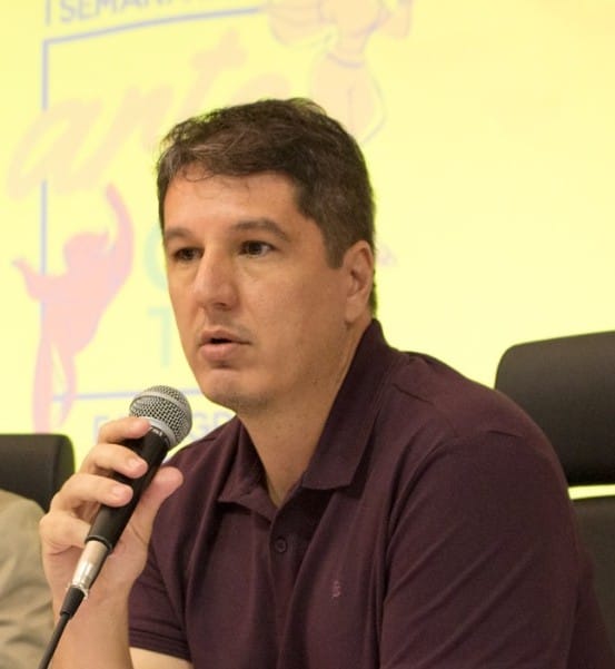 Professor Iúri Ribeiro com microfone na mão durante evento escolar 