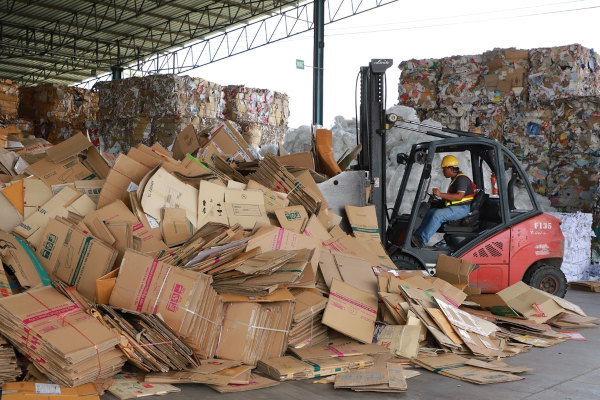 Homem dirigindo uma empilhadeira em um depósito de reciclagem.