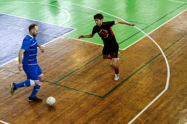 Jogadores em uma quadra de futsal com o piso de madeira. 
