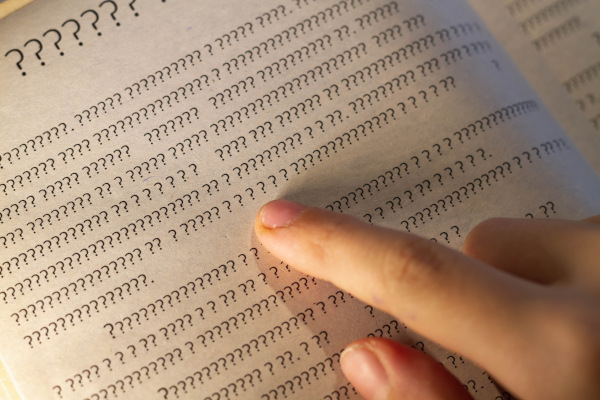 Mão sobre texto formado apenas por interrogações em uma folha de papel, em alusão ao analfabetismo.