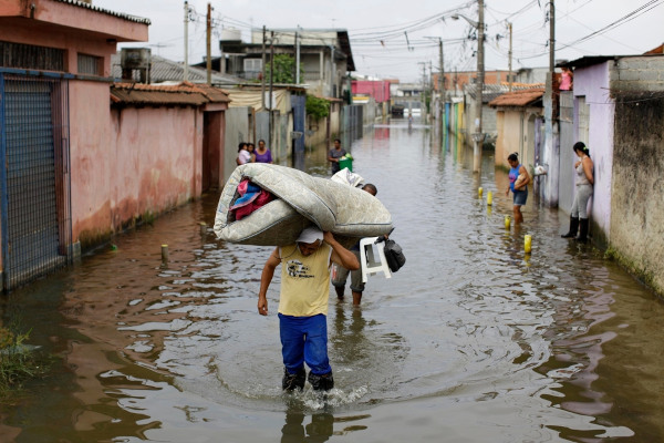 Pessoas carregando seus pertences em enchente causada por chuvas volumosas, um dos impactos do aquecimento global no Brasil.