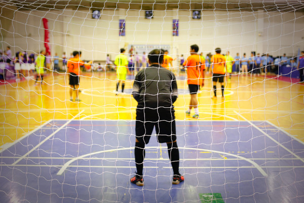 Times adversários jogando futsal, com ênfase no goleiro de um dos times.