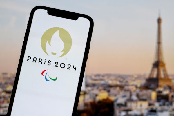 Celular com a logo das Paralimpíadas de Paris 2024 na região urbana de Paris, na França, com a Torre Eiffel desfocada ao fundo.