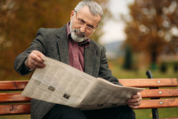 Homem lendo um jornal, alusão ao principal veículo de comunicação para a publicação de reportagens.