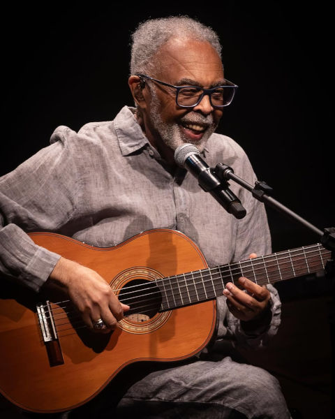 Gilberto Gil, um dos maiores nomes da música brasileira, sorrindo com violão em apresentação musical.