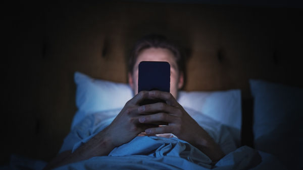 Homem usando celular na cama, uma das causas do brain rot.