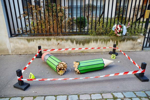 Lápis quebrado cercado por uma faixa de perícia em referência ao atentado contra a revista Charlie Hebdo.