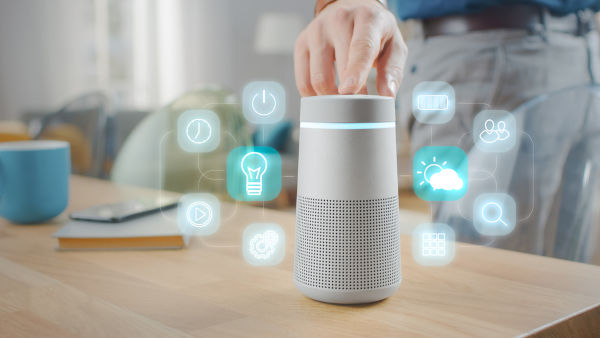 Mão tocando em um dispositivo de assistência virtual, liberando ícones de tecnologia.