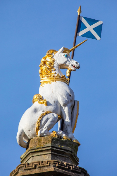 Escultura de um unicórnio branco ao lado de uma pequena bandeira da Escócia.