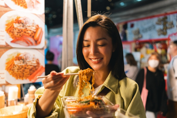 Mulher chinesa comendo macarrão com hashi, evidenciando a culinária como um dos elementos da cultura.