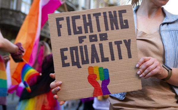 Mulher segurando placa com escrito “Fighting for equality”, em texto sobre orientação sexual.